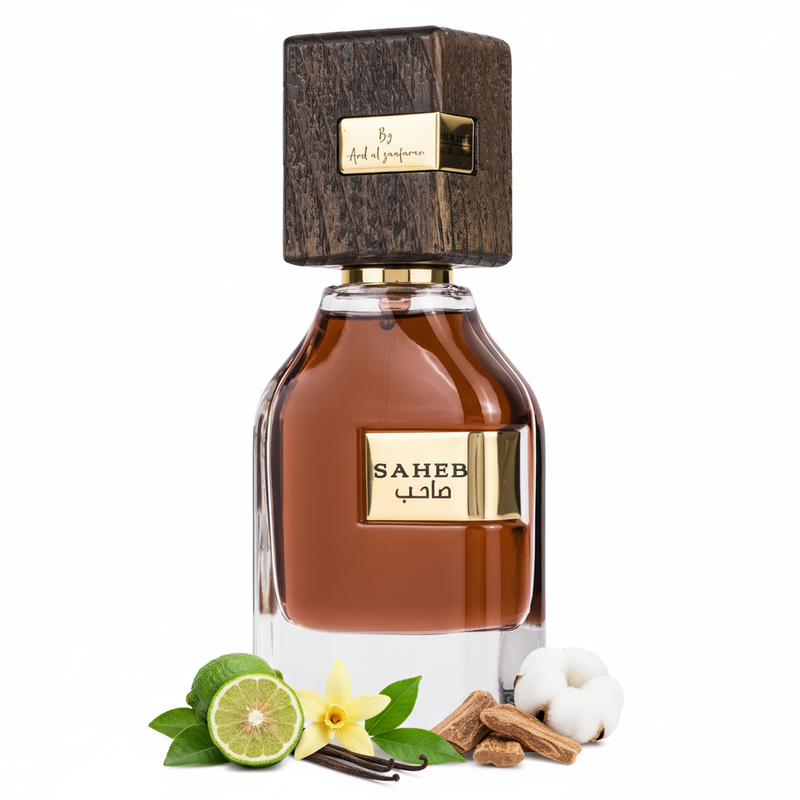 Frasco de perfume Saheb de Ard Al Zaafaran EDP, botella cuadrada redondeada en vidrio transparente con líquido coñac-ámbar en la mitad superior y vidrio claro en la inferior, placa dorada con texto SAHEB y caligrafía árabe صاحب, anillo dorado en cuello y gran tapa cuadrada de madera oscura nogal con placa dorada By Ard al zaafaran, sobre fondo blanco, rodeado de bergamota, vainilla, pachulí, madera de oud y almizcle.