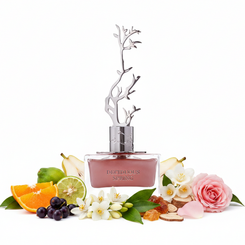 Frasco Deciduous Spring EDP, botella rectangular ancha y plana en vidrio transparente con líquido rosa polvoriento en la parte inferior, texto DECIDUOUS SPRING minimal, cuello cilíndrico cromo plateado, tapa escultórica espectacular de árbol desnudo en ramas cromo plateado 3D, rodeado de mandarina, bergamota, grosellas negras, pera, rosa, azahar, jazmín sambac, fresia, pachulí, amberwood y madera de cachemira.